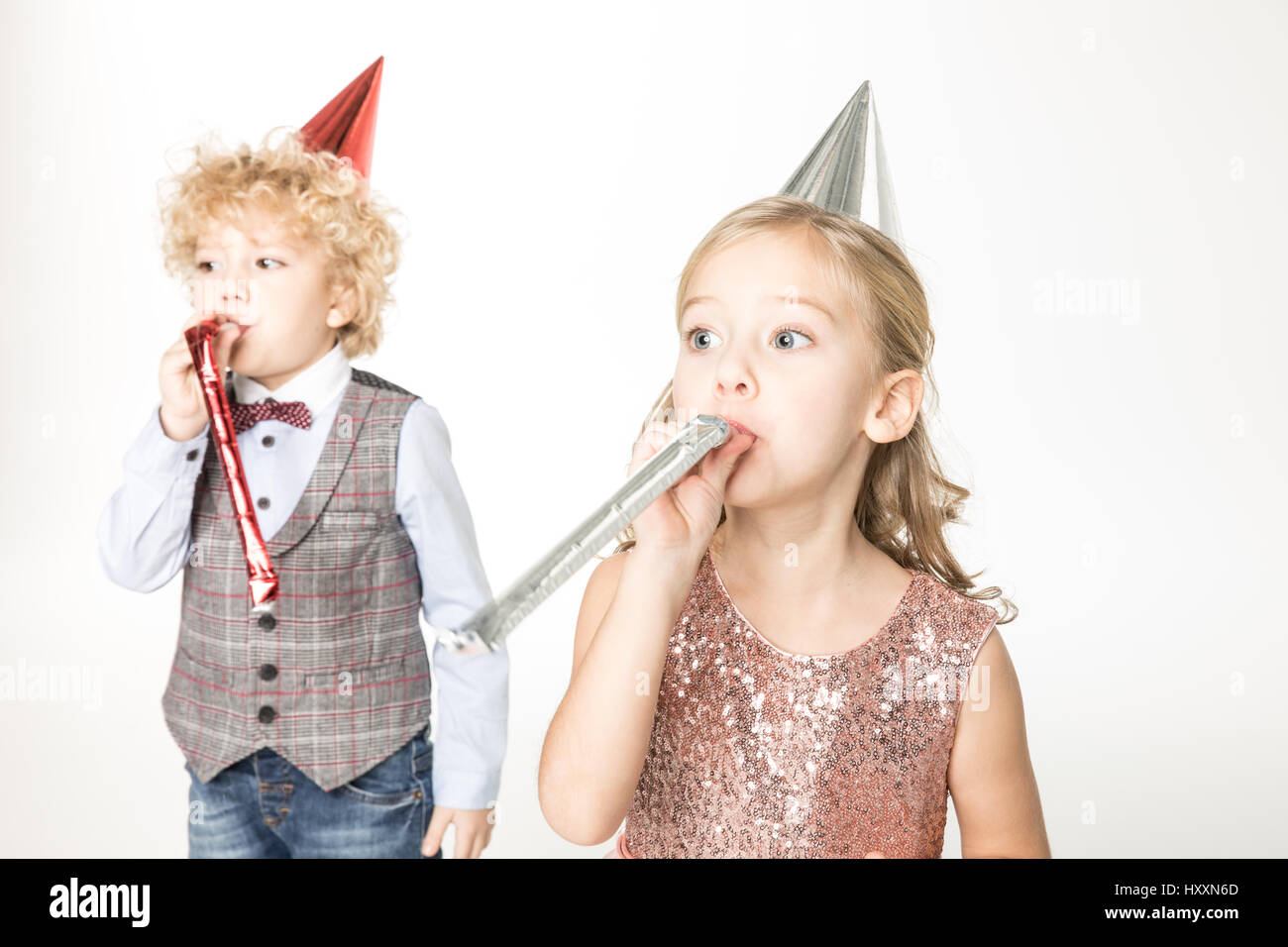 Little boy and girl in cone hats having fun with party blowers Stock ...