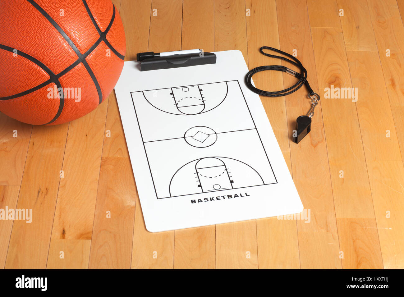 A basketball with coach's clipboard and whistle on a wooden gymnasium floor Stock Photo