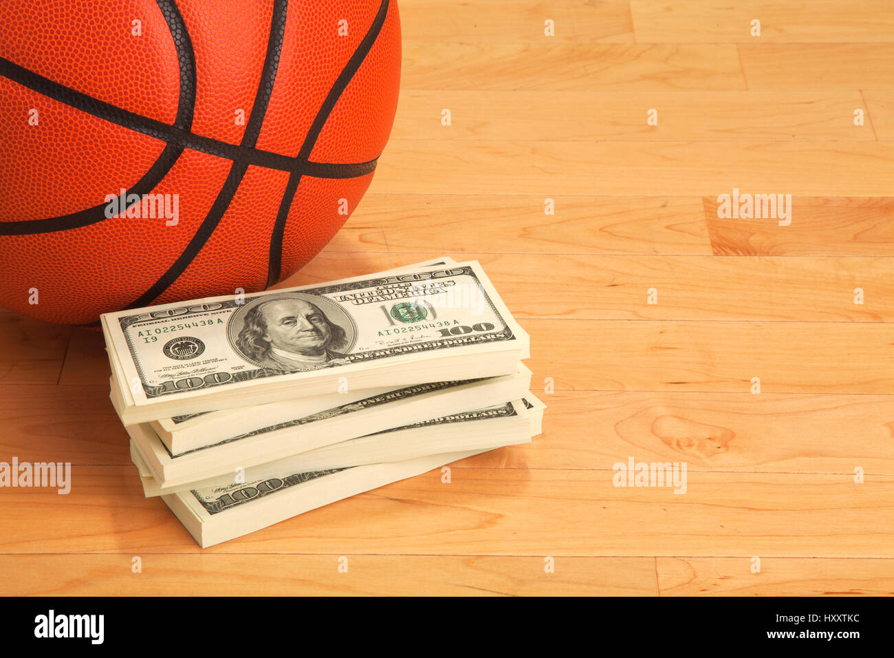 Basketball and stack of one hundred dollar bills on wooden court floor Stock Photo