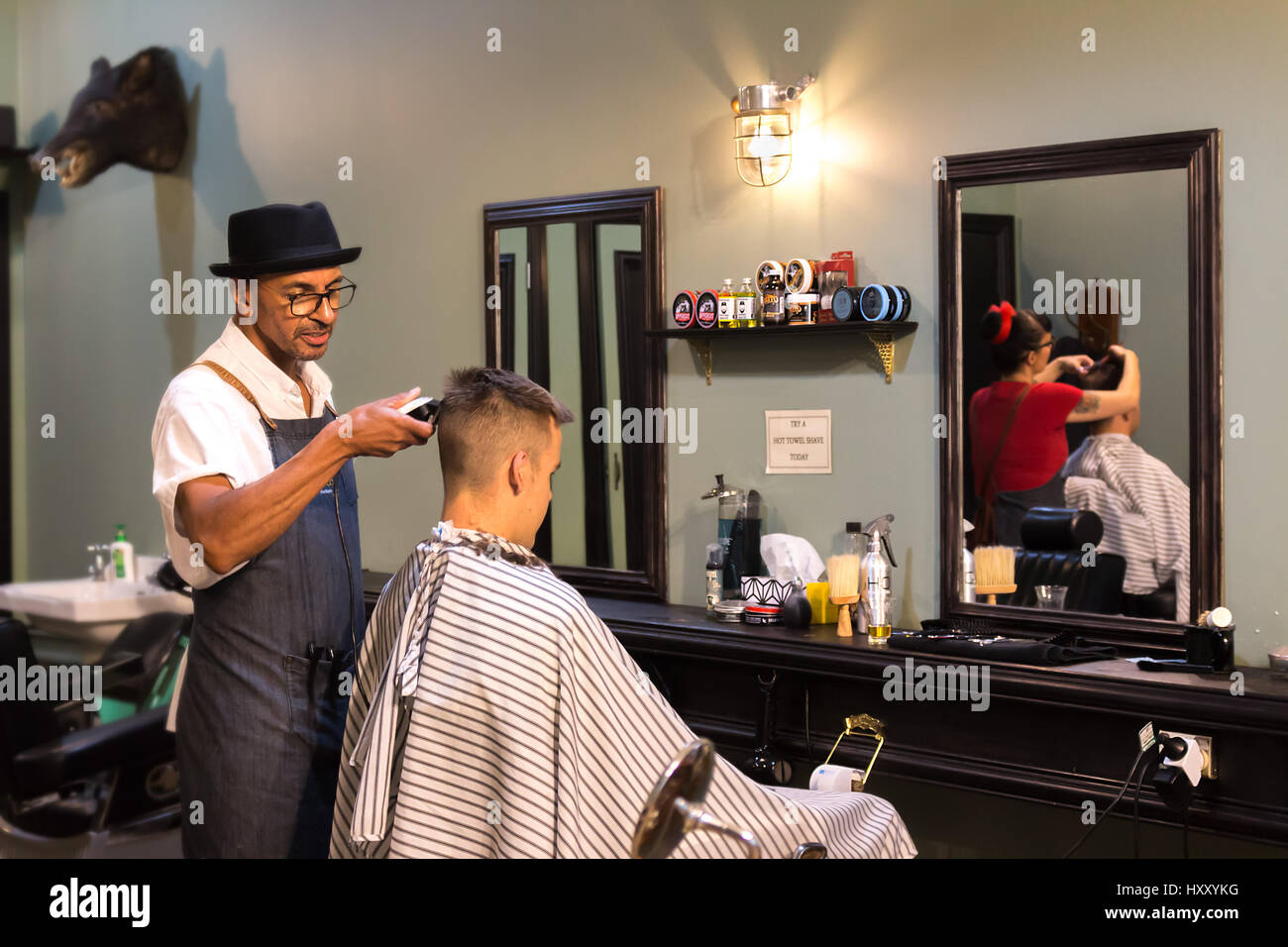 Auckland - February 17, 2017: A barber is making a haircut with a clipper for a customer, inside a retro style barbershop. Stock Photo
