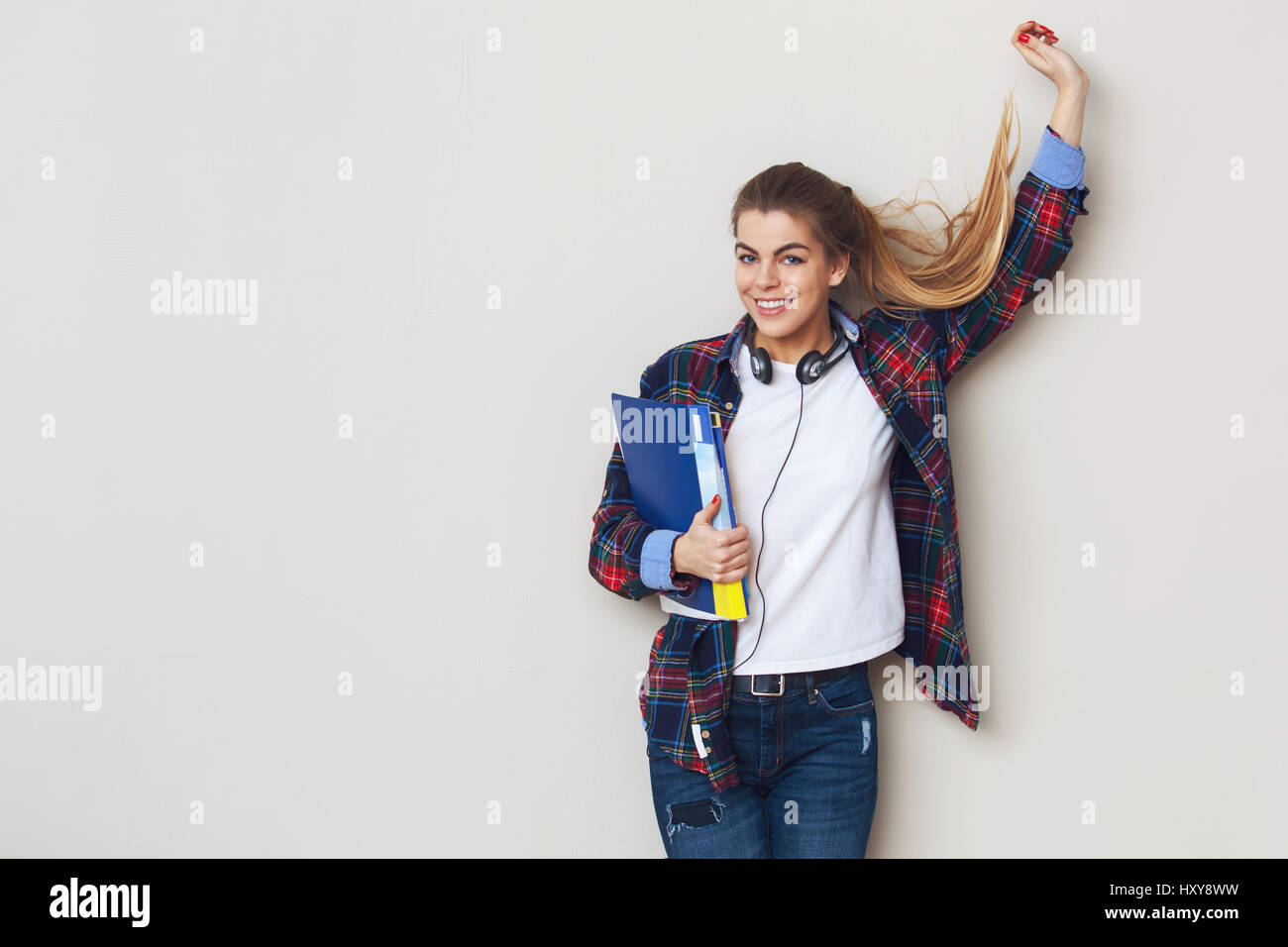 Studio portrait of young beautiful female student with books standing ...