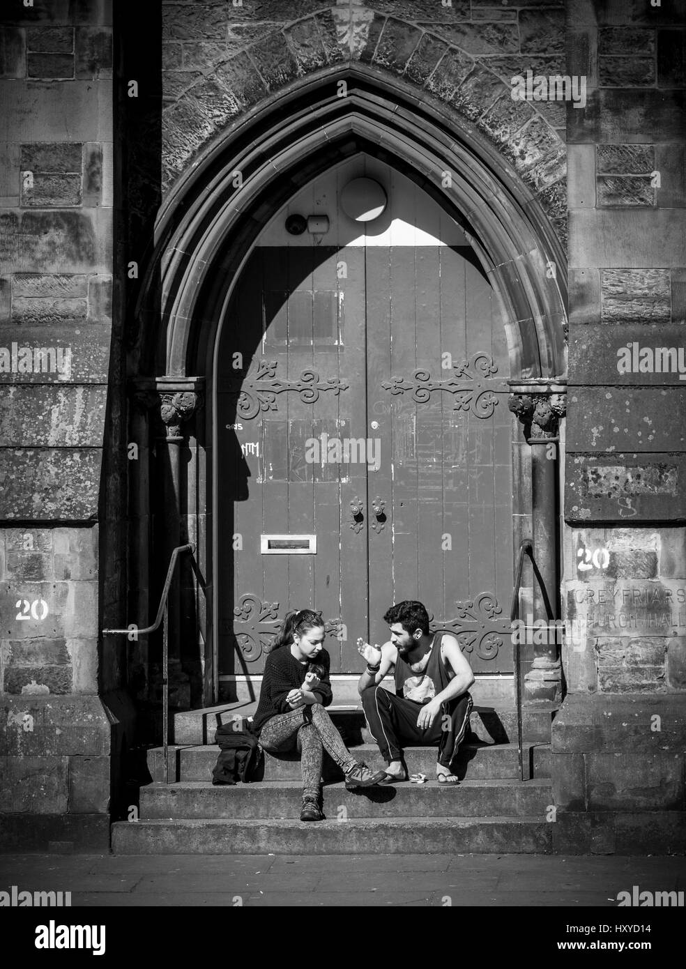 Male and female couple sat on steps of church entrance talking and smoking Stock Photo