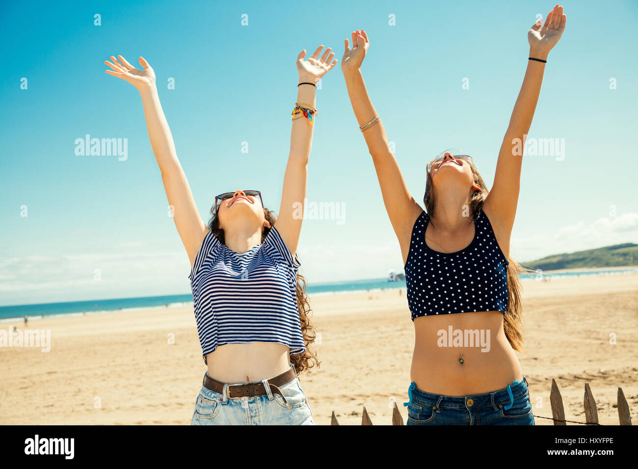 Funny girl friends with arms outstretched greeting the sun on the beach