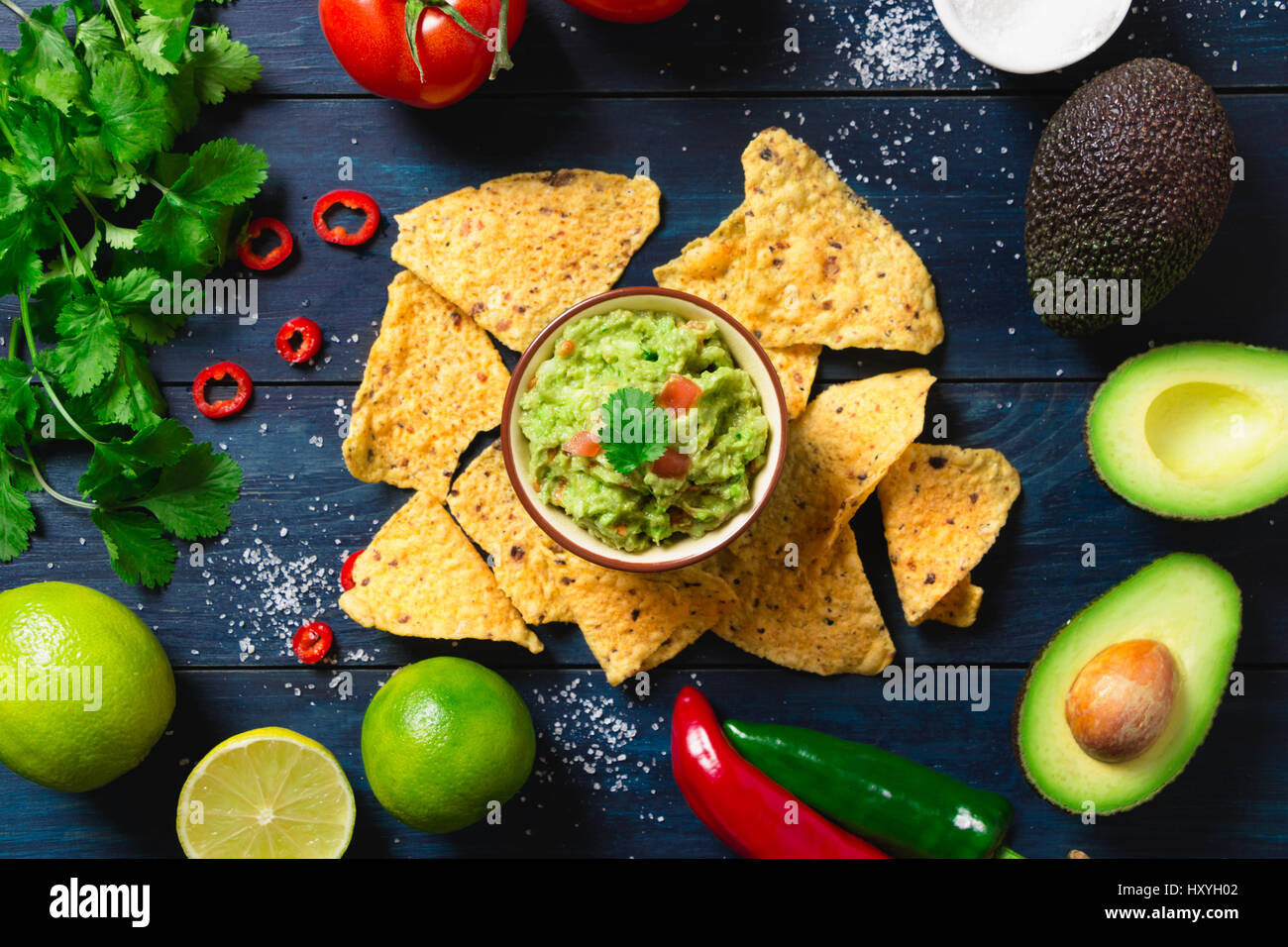Guacamole bowl with ingredients and tortilla chips on a blue painted wooden table. Top view Stock Photo