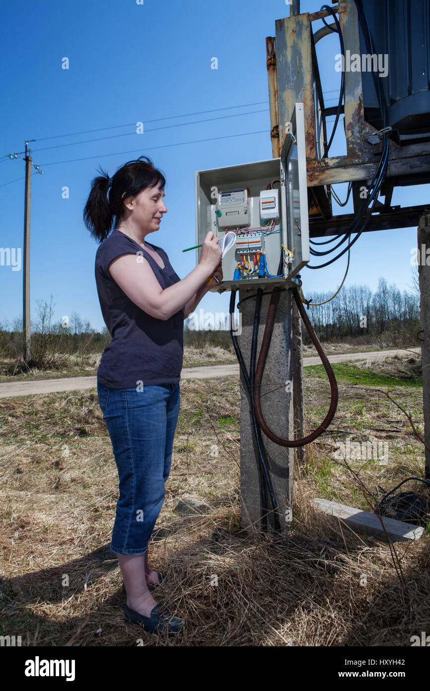 Woman checking electric meter reading, standing near electricity