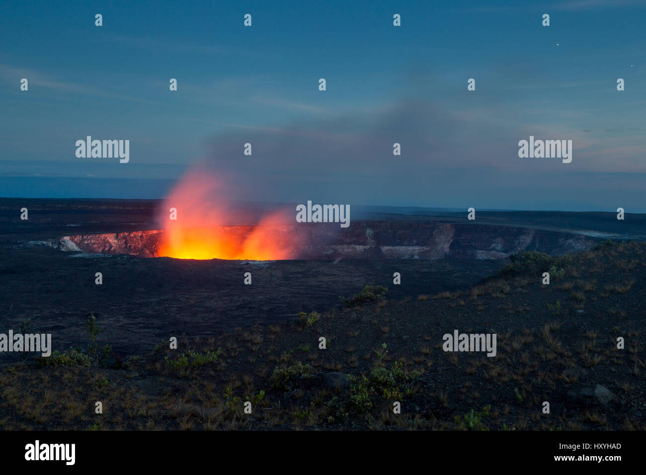 An active lava lake inside the Halemaumau Crater on Kilauea illuminates volcanic steam rising up in front of the night sky on Big Island, Hawaii, USA. Stock Photo