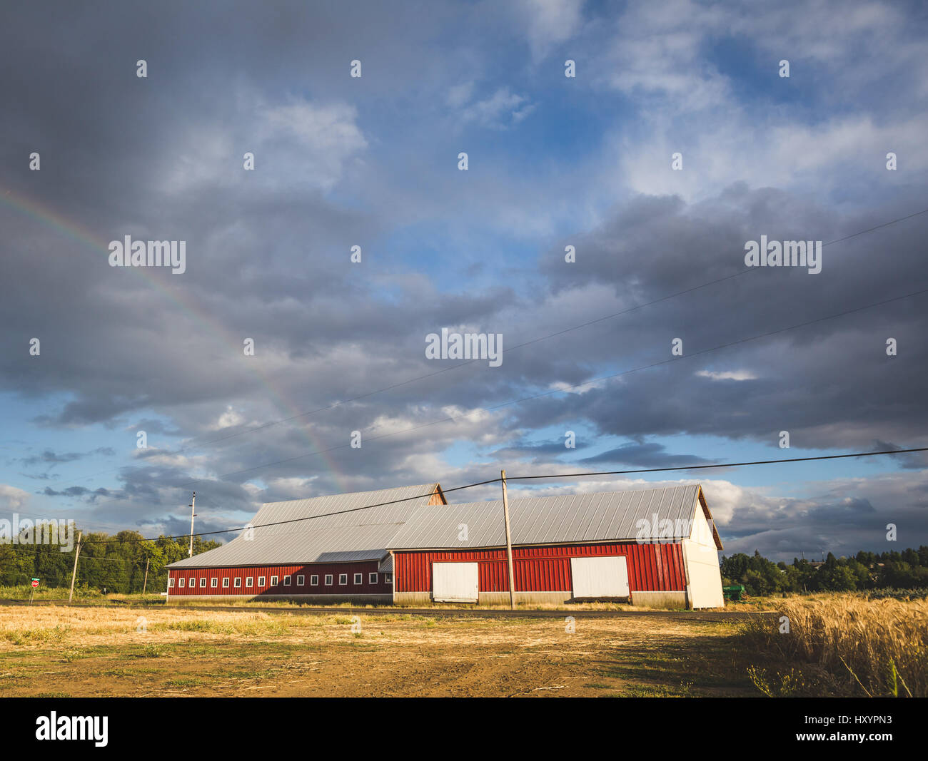 Red barn building with modern design and red walls under cloudy skies with a rainbow. Oregon, USA. Stock Photo