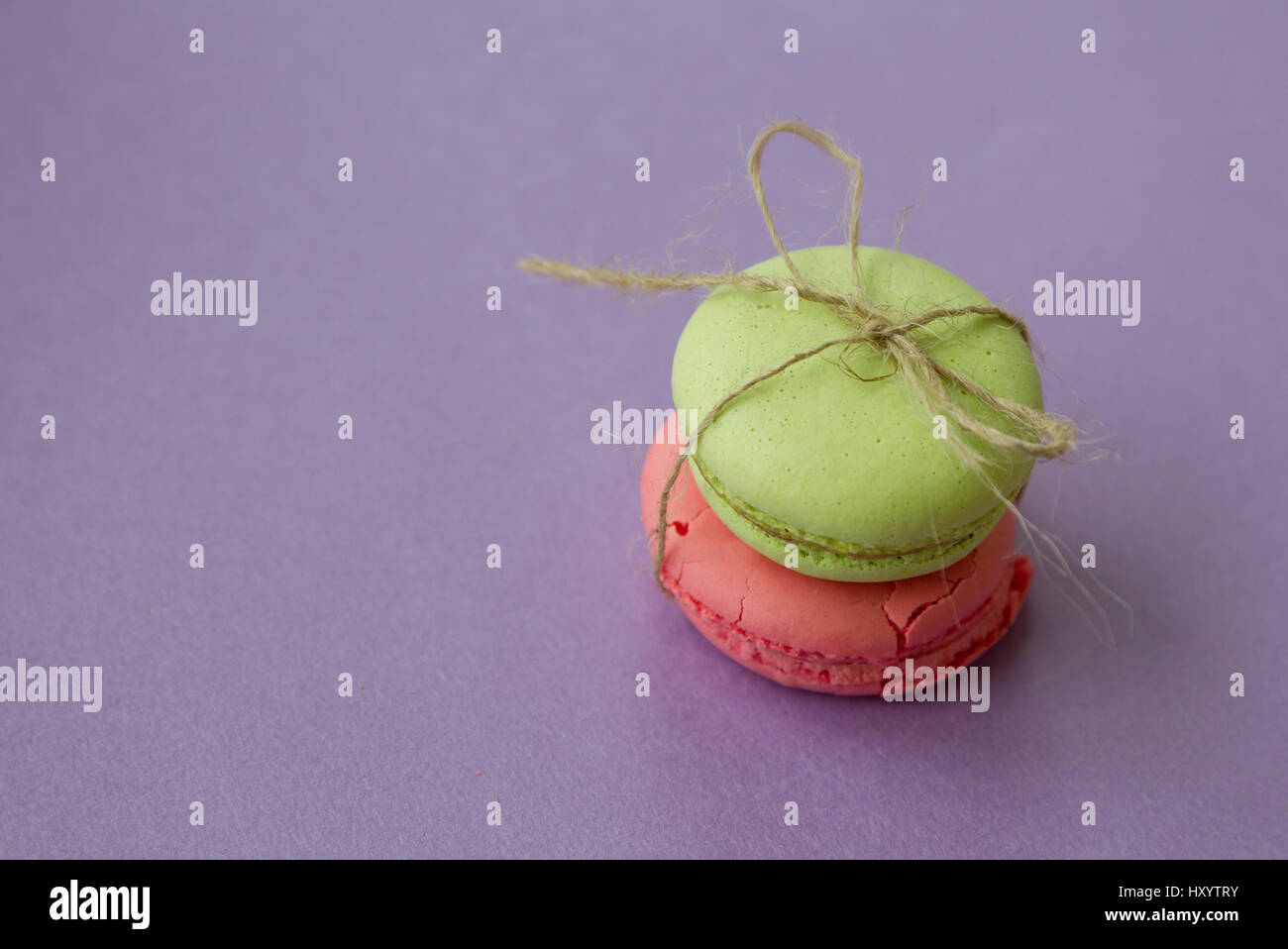 Two macaroons with bow from natural rope on purple background with copy ...