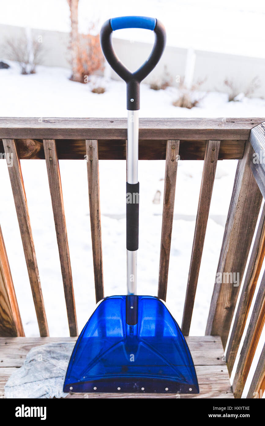Blue, silver, and black snow shovel on back porch of home in winter. Stock Photo
