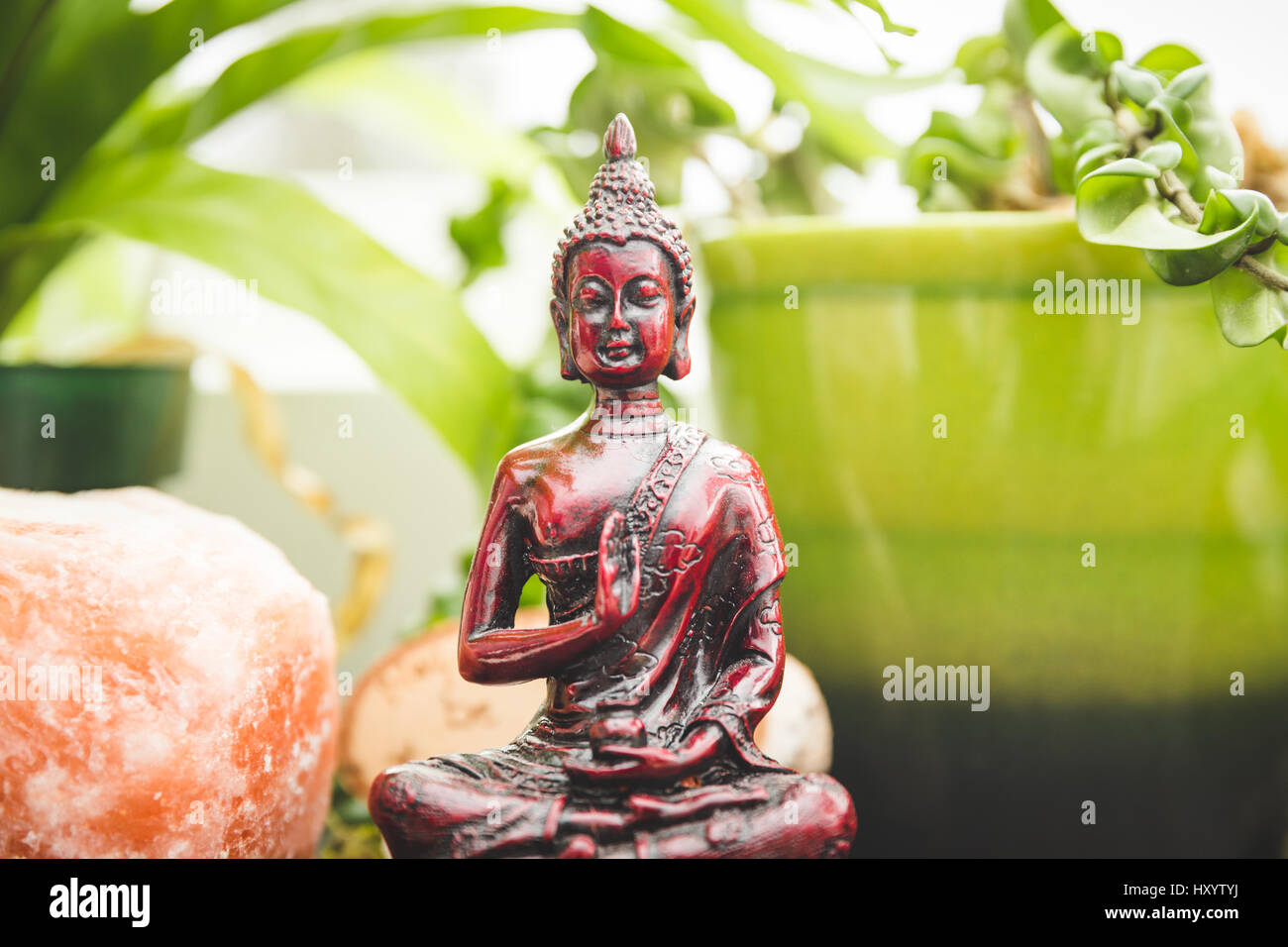 Religious figure or sculpture, plants, crystal salt rock, and other decorations on a shelf or bookcase. Stock Photo