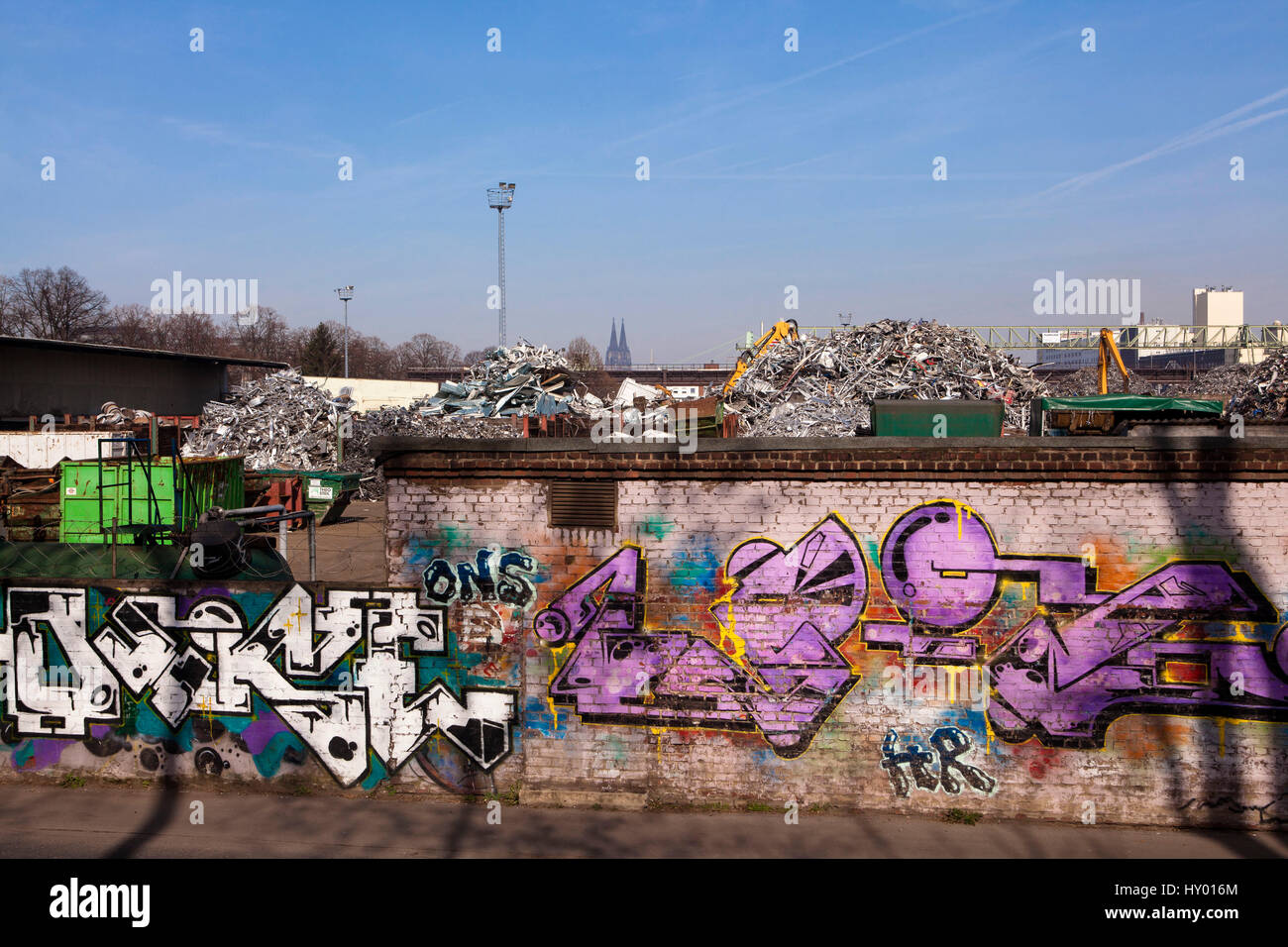 Germany,  Cologne, scrap yard with old metal in the district Deutz, in the background the cathedral, wall with graffiti. Stock Photo