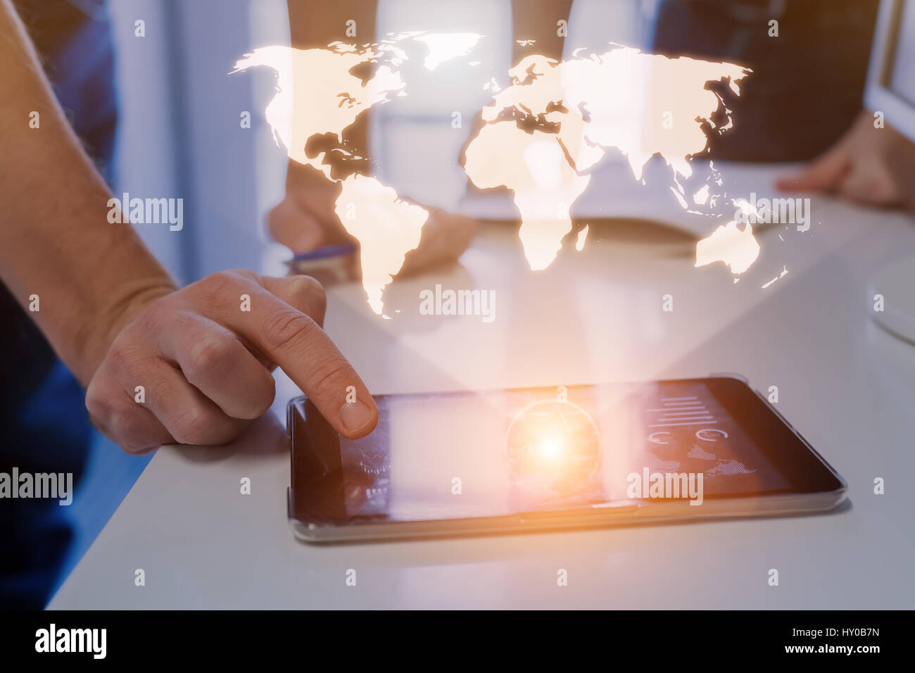 Global business concept with a world map hologram above a digital tablet and a team of two businessmen in background Stock Photo