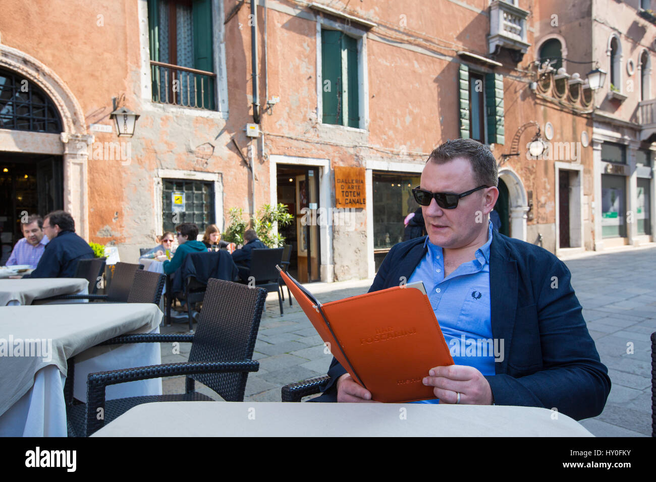man sitting outside a restaurant reading a menu Stock Photo
