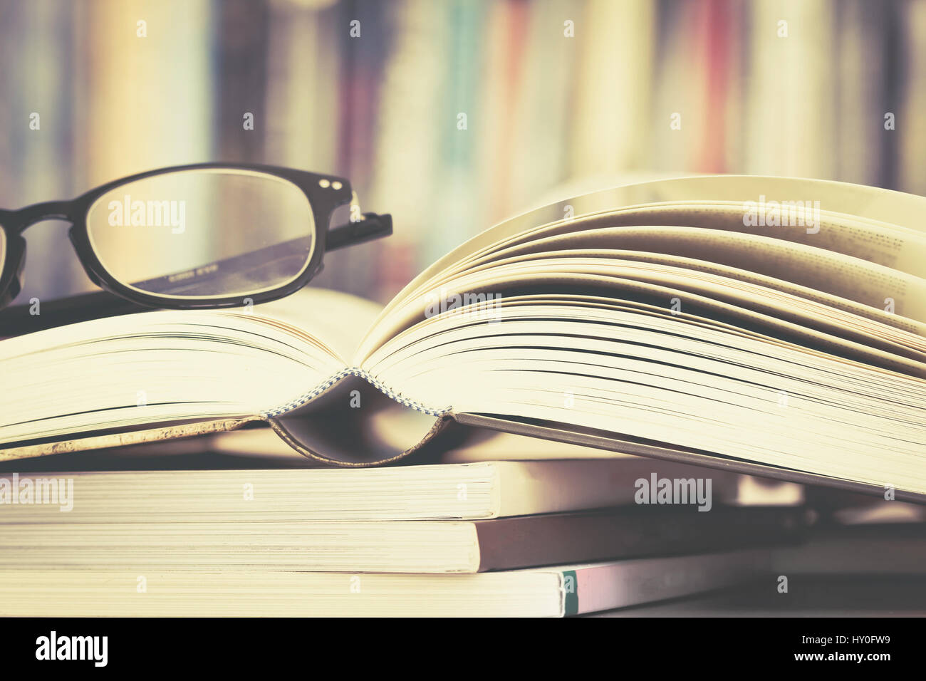 Close up opened book page and reading eyeglasses with blurry bookshelf