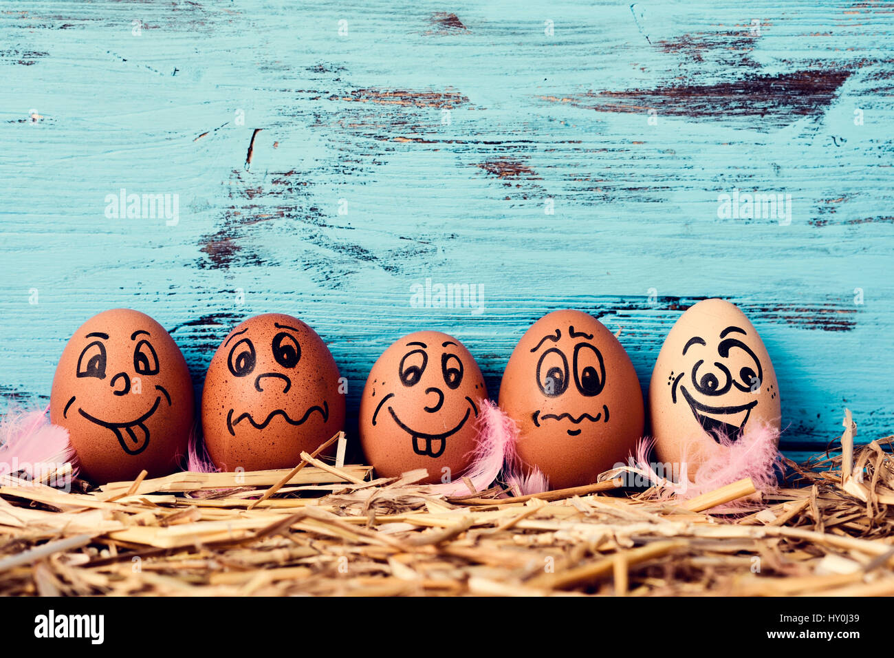 Some Brown Eggs With Funny Faces On A Pile Of Straw Against Blue Rustic Wooden Background Blank Space Above Them