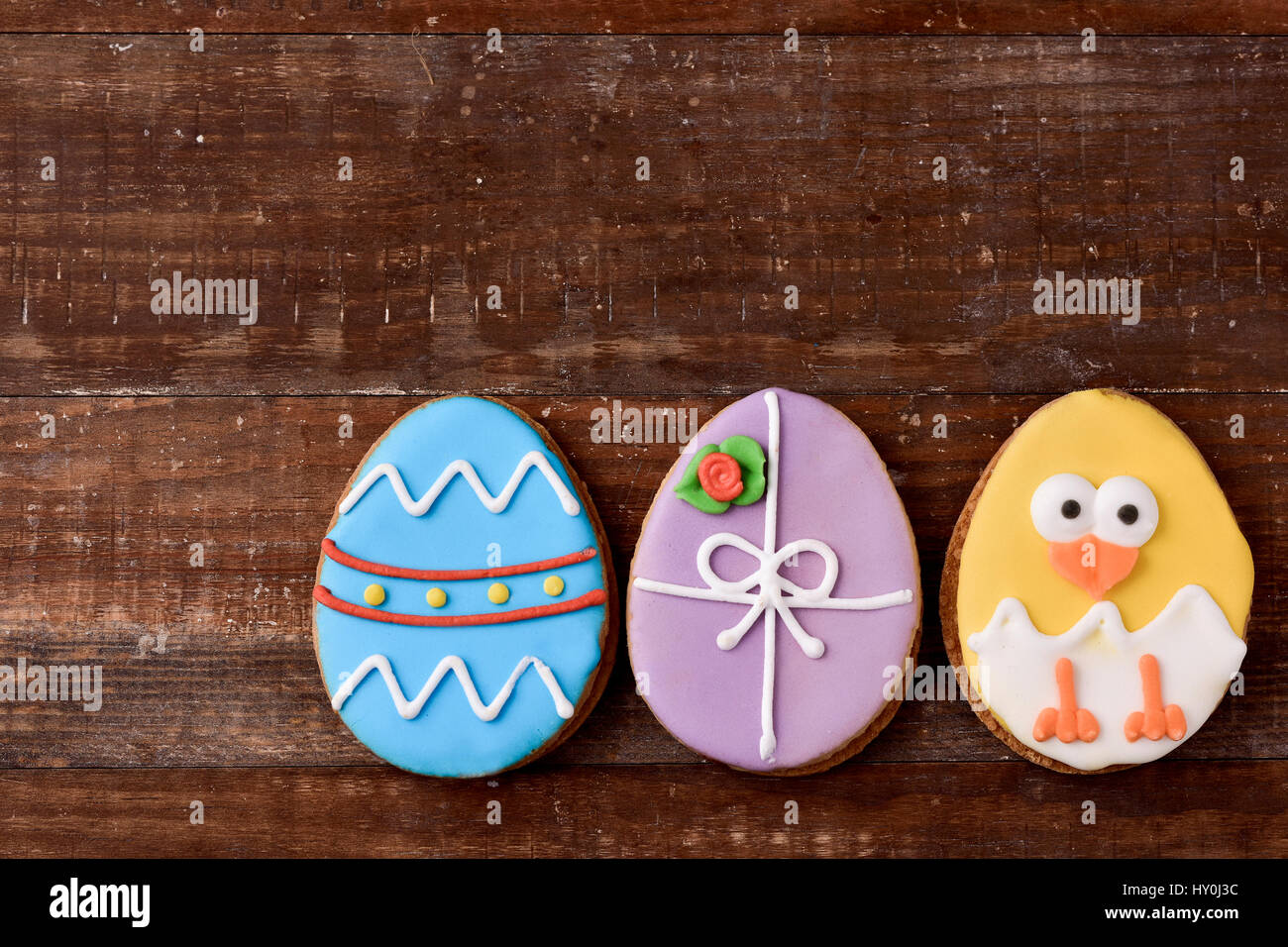 a pile of some different handmade cookies patterned as decorated easter eggs and as a funny chick against a rustic wooden background, with a blank spa Stock Photo