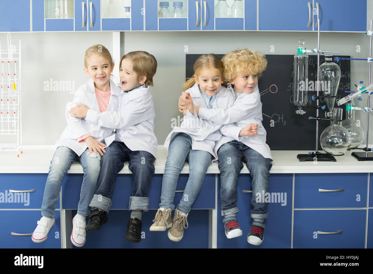 Schoolchildren in lab coats sitting together in chemical laboratory Stock Photo