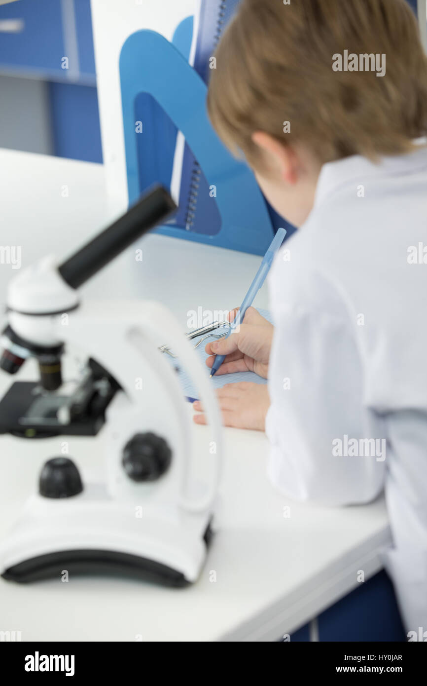 Schoolboy in white lab coat taking notes during scientific experiment ...
