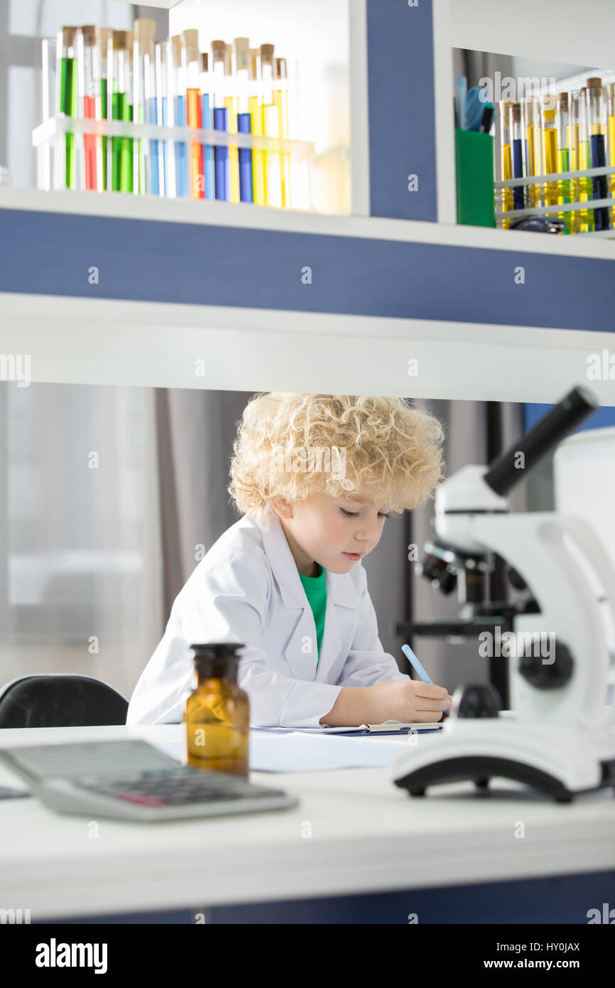 Schoolboy in white lab coat taking notes during scientific experiment ...