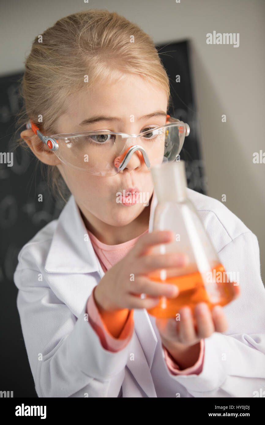 Exited girl wearing lab coat and protective glasses holding flask with