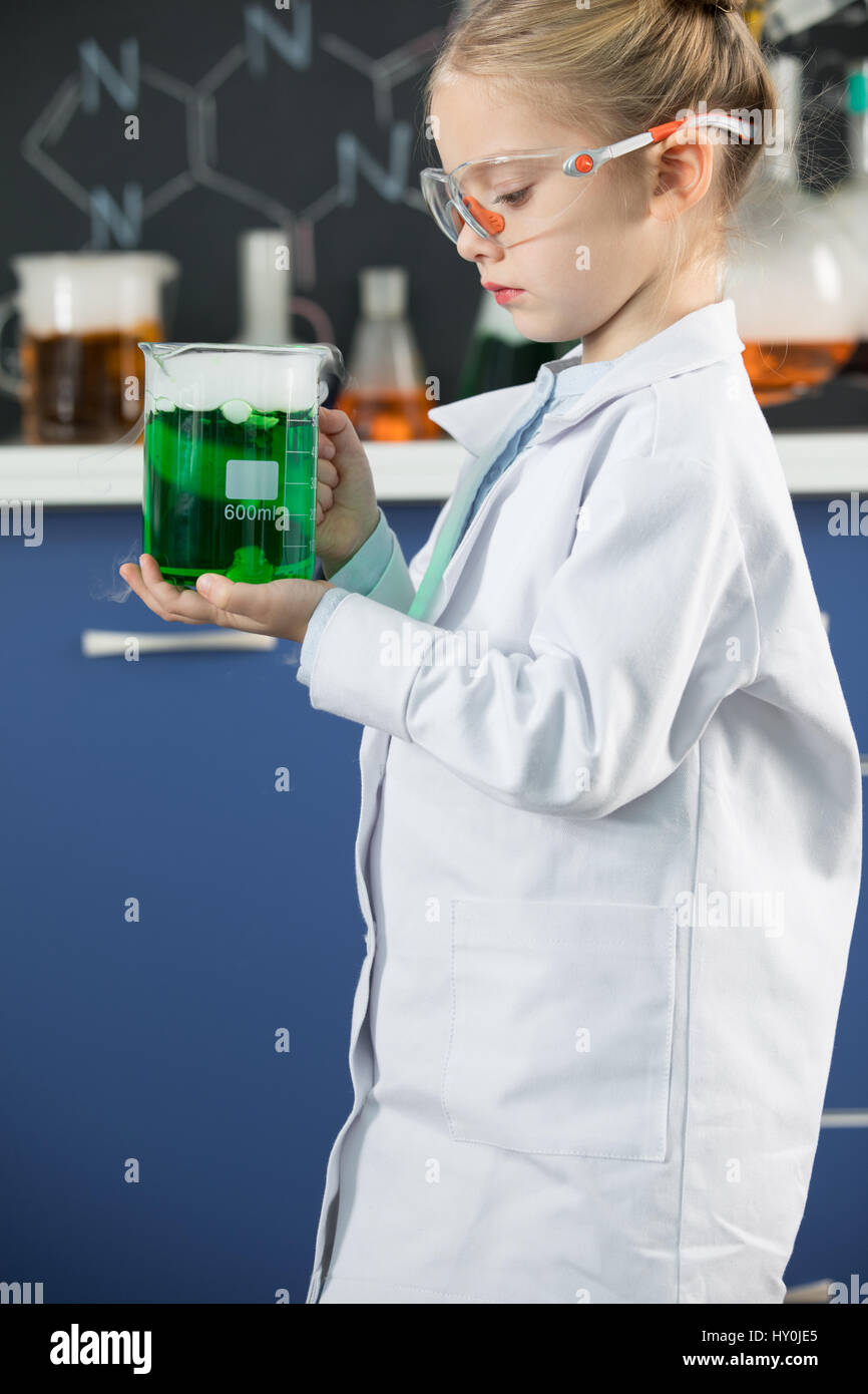 Little girl wearing lab coat and protective glasses holding flask with