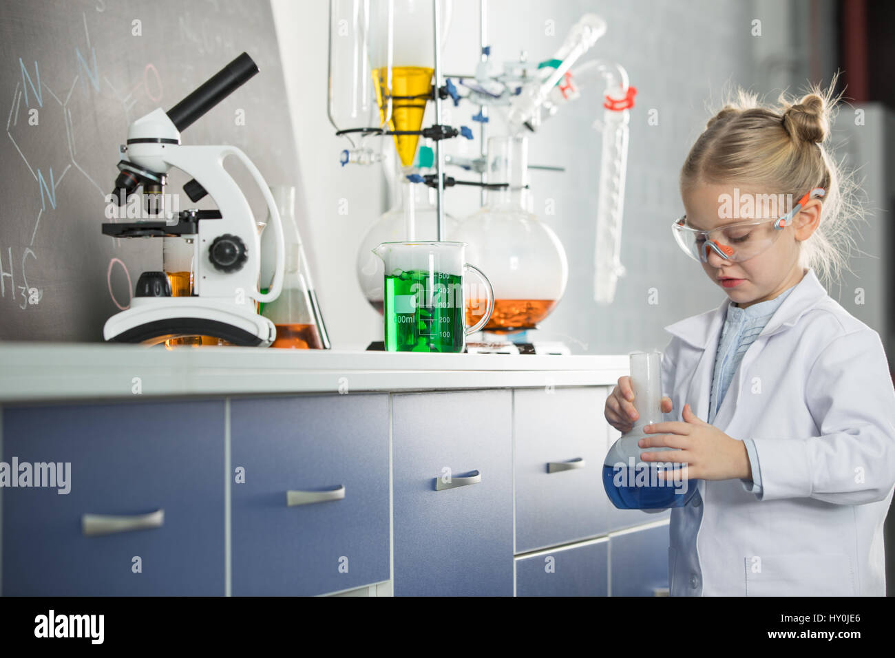 Little girl wearing lab coat and protective glasses holding flask with