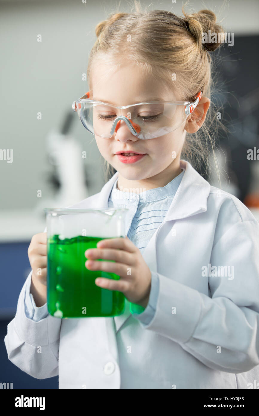 Little girl wearing lab coat and protective glasses holding flask with