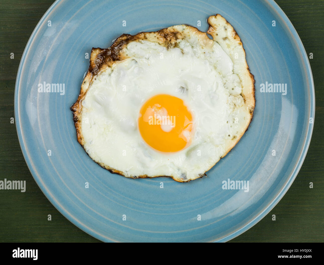 Single Fried Egg on a Blue Plate Against a Green Background Stock Photo