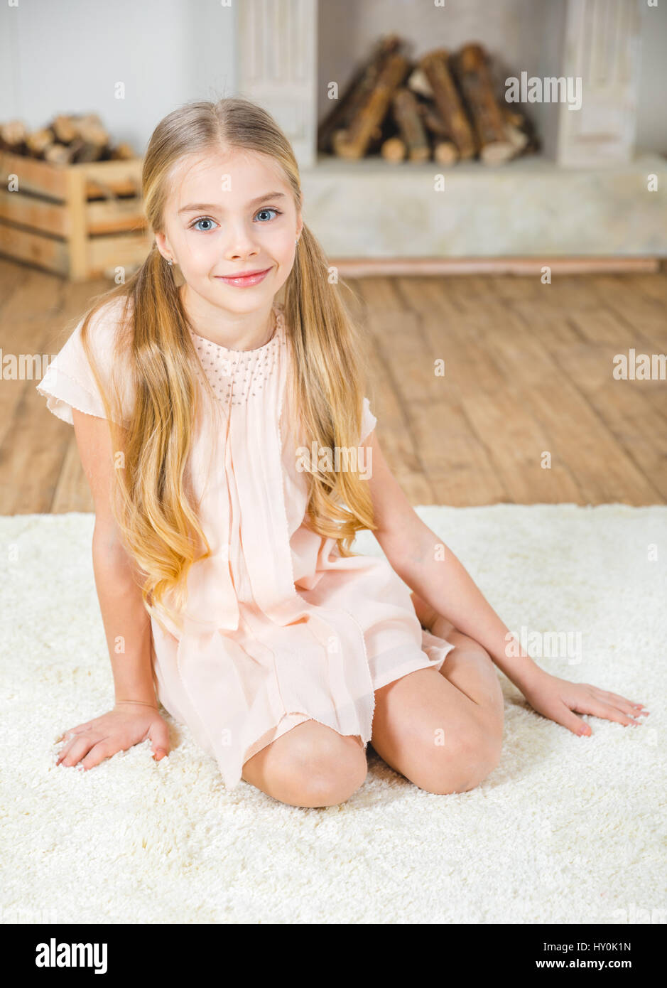 Cute little girl sitting on white carpet and smiling at camera
