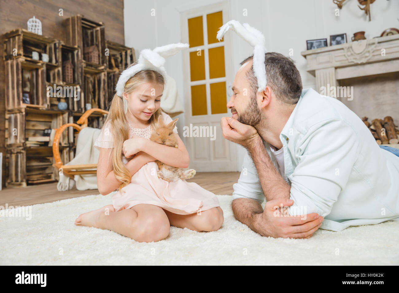 Happy father and daughter in bunny ears playing with rabbit at home ...