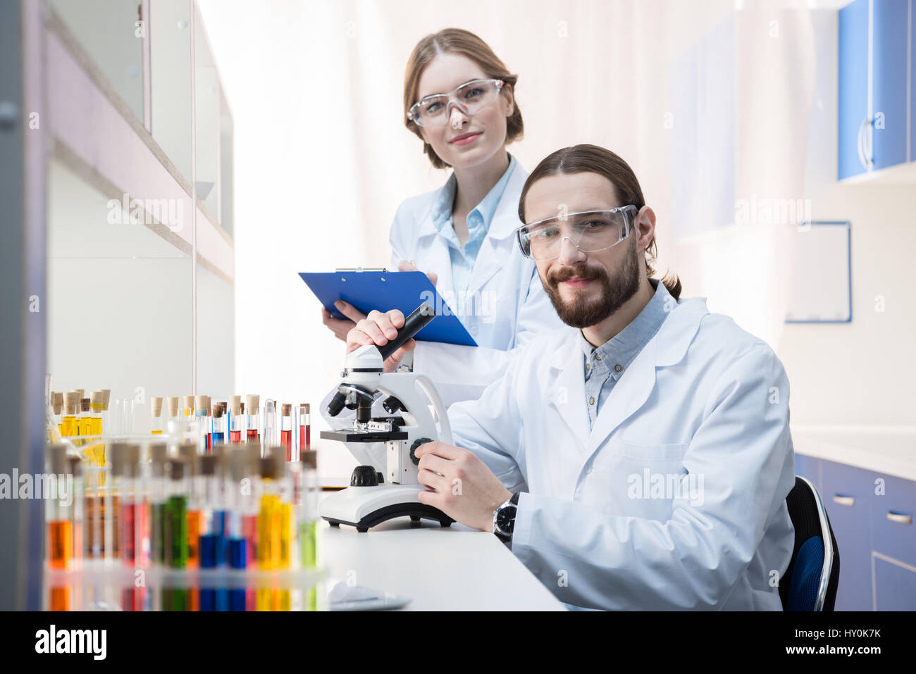 Microchemists Two smiling chemists working with microscope and taking notes in ...