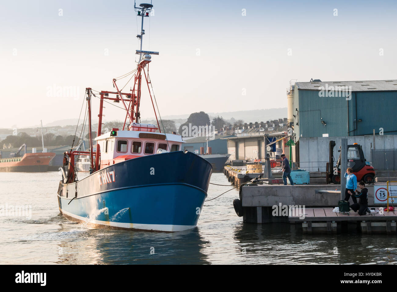 A Teignmouth trawler, docking to unload its catch of fish on the fish quay at Teignmouth, Devon, UK. Two young males are fishing on a pontoon also. Stock Photo