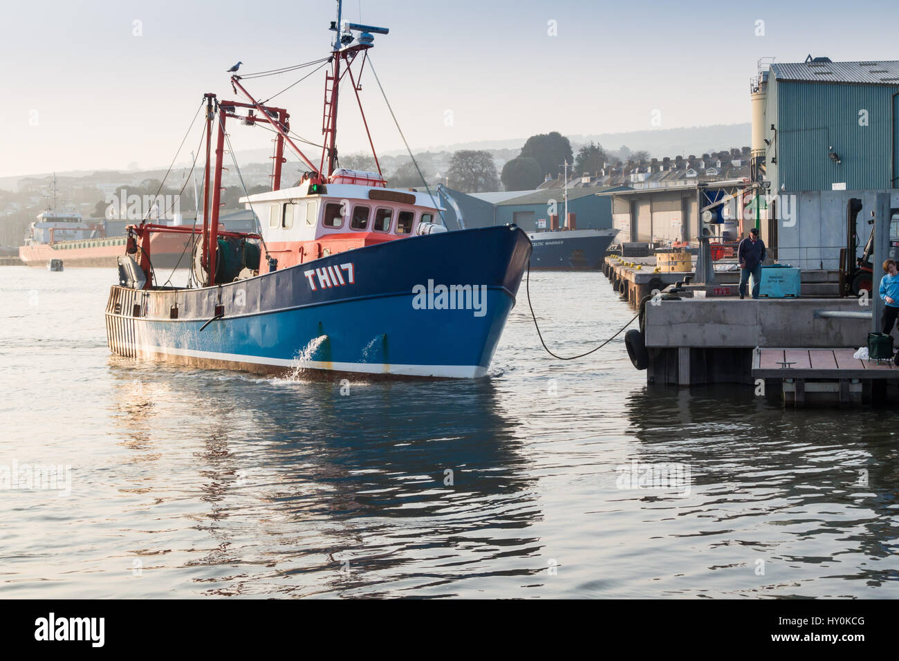 A Teignmouth trawler, docking to unload its catch of fish on the fish quay at Teignmouth, Devon, UK. Two young males are fishing on a pontoon also. Stock Photo