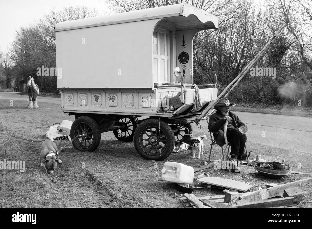 Elderly traveller and his horse and two dogs sit outside his traditional wagon by a brazier Stock Photo