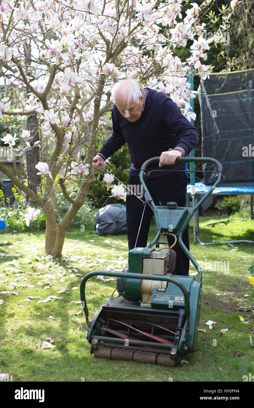 Elderly pensioners trying to start a petrol lawn mower in a English residential garden on a