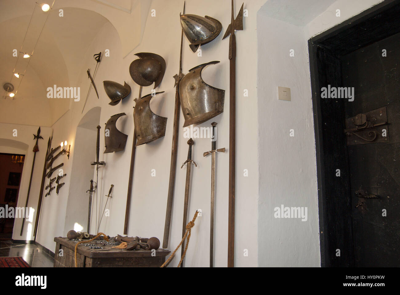 Medieval helmets, cuirass, swords, pistols and halberds as decoration in an interior of an old manor house. Wooden door with wrought-iron lock. Stock Photo