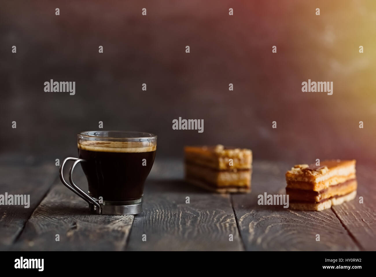 Glass cup of black coffee and two caramel nut cake slices on wooden table. Dark food photography Stock Photo