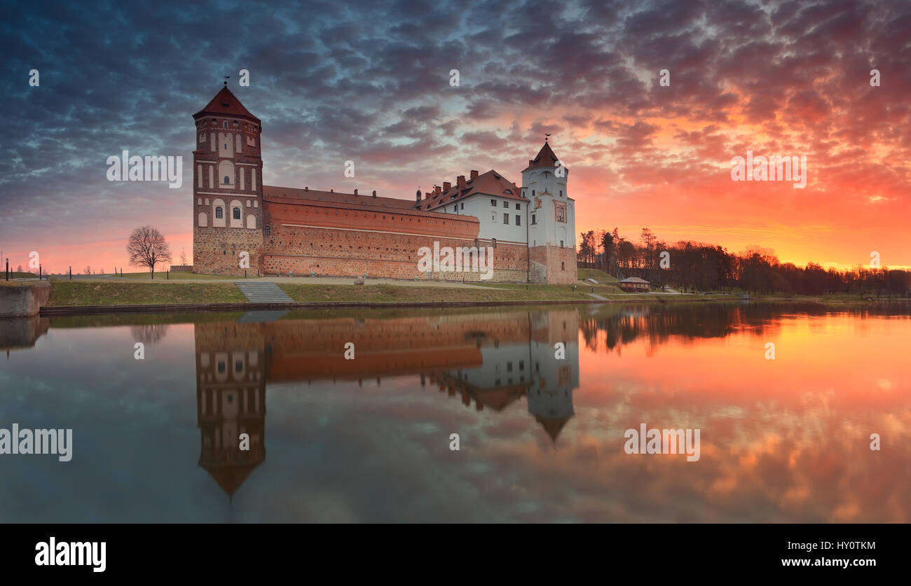 Castle on sunrise background reflect in lake. Beautiful sunrise over lake. Sky white red yellow clouds in the morning. Stock Photo