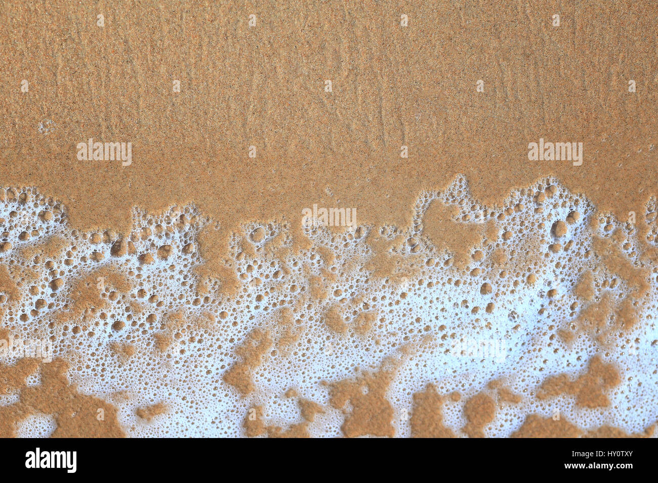 Sea foam on yellow sand from above. Good vacation background. Sea foam on sand background close-up. Copy space on sea sand background. Stock Photo