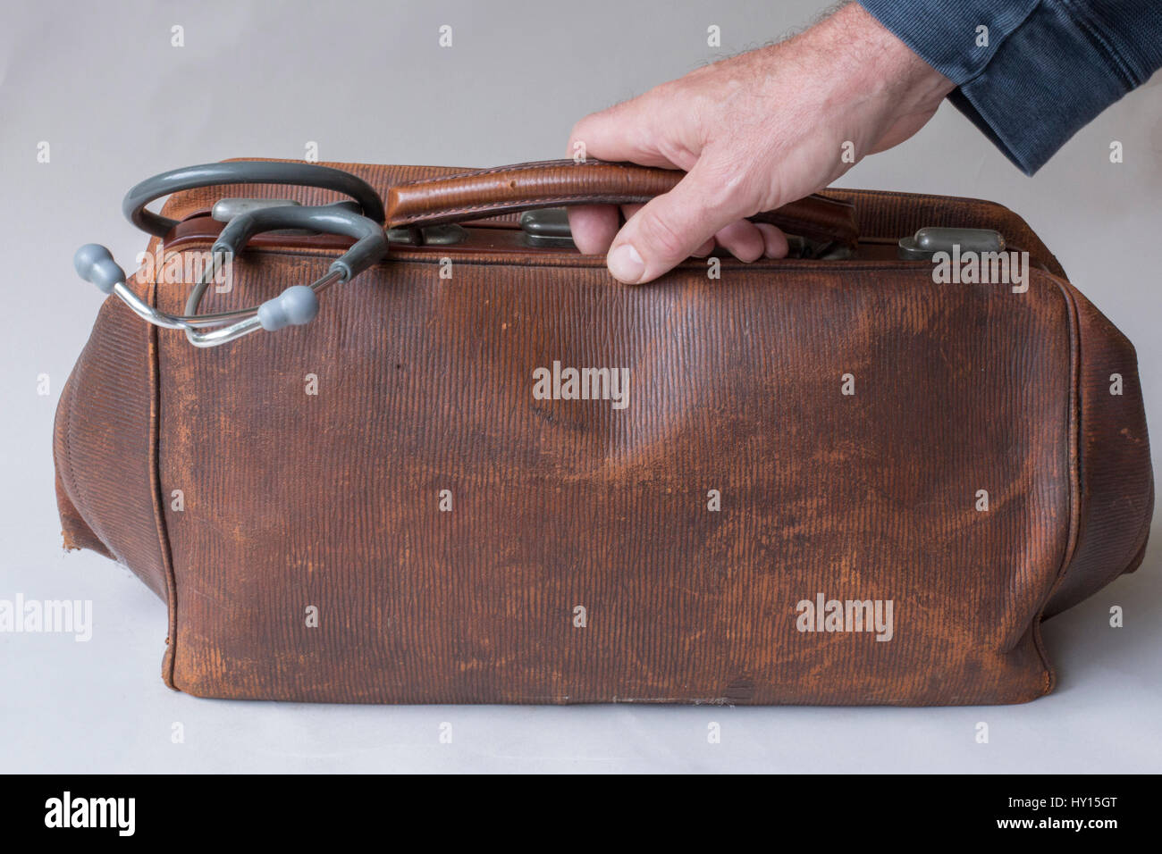 Hand of doctor holding vintage brown leather case with stethoscope