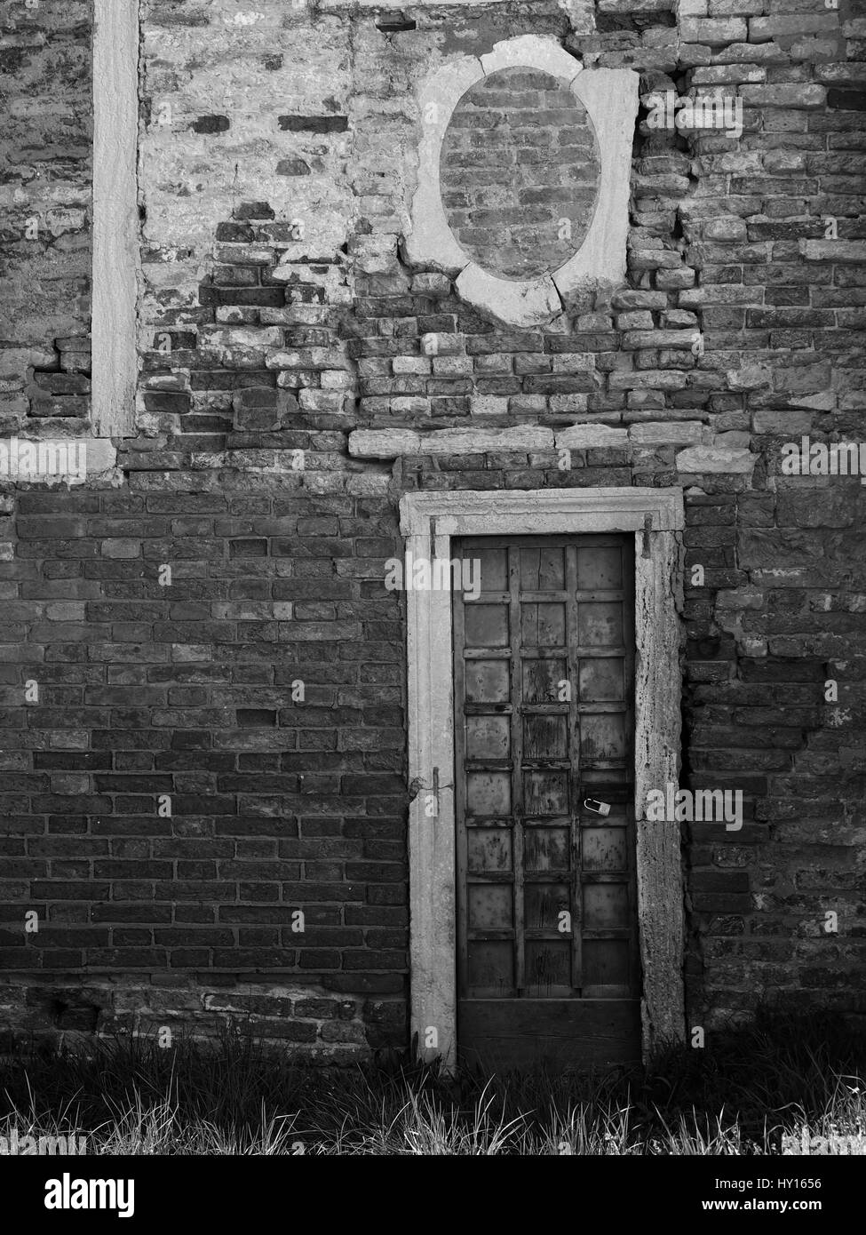 Old wooden paneled door with peeling paint and rusting hinges in an ancient brick wall Stock Photo