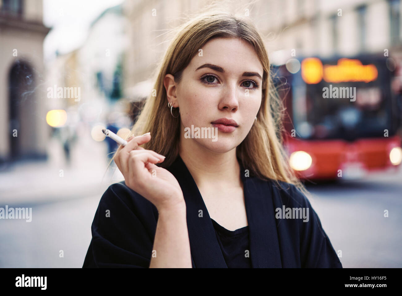 Sweden, Uppland, Stockholm, Kungsholmen, Portrait of young woman smoking in street Stock Photo