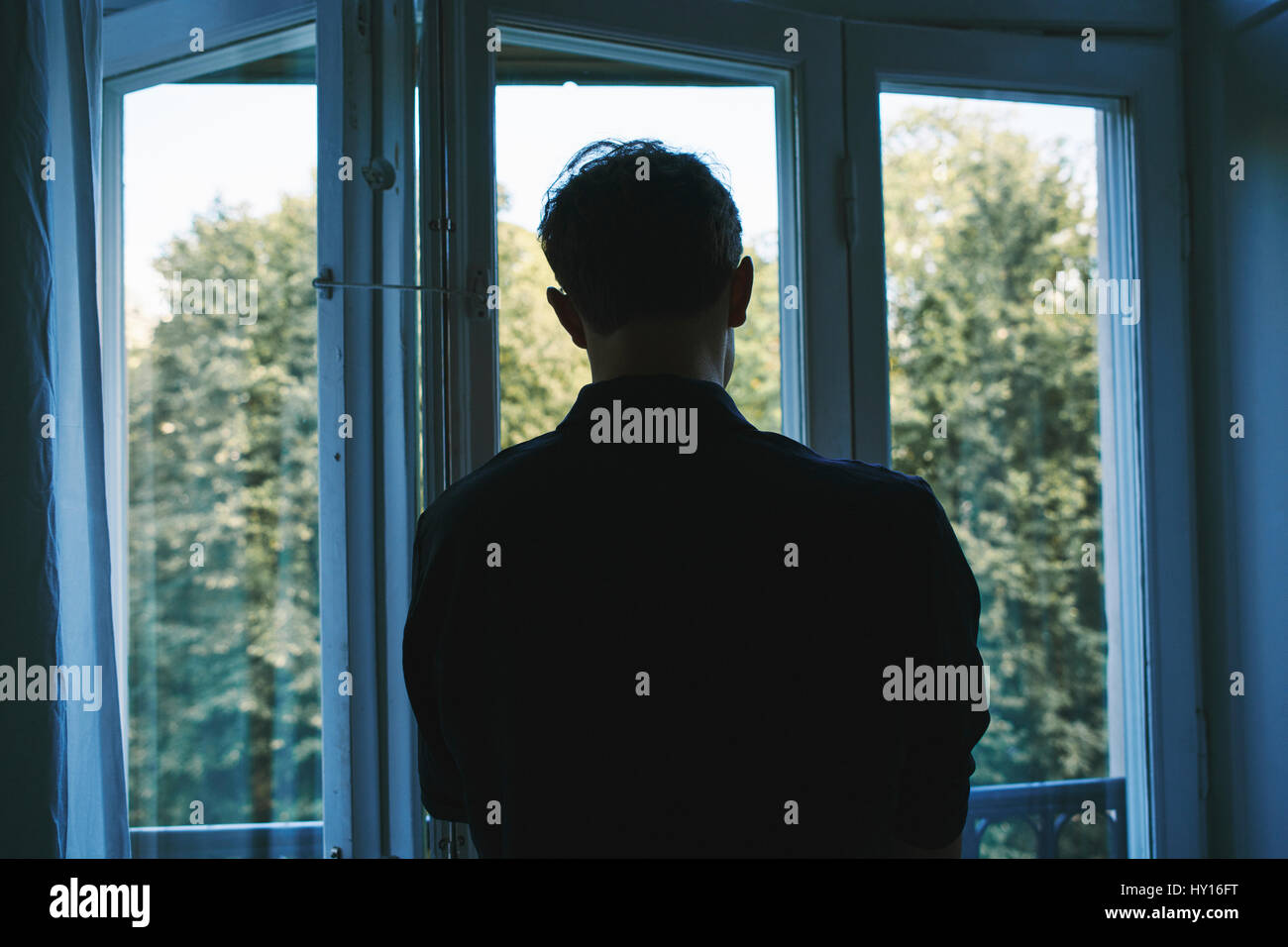 Sweden, Young man looking through window Stock Photo