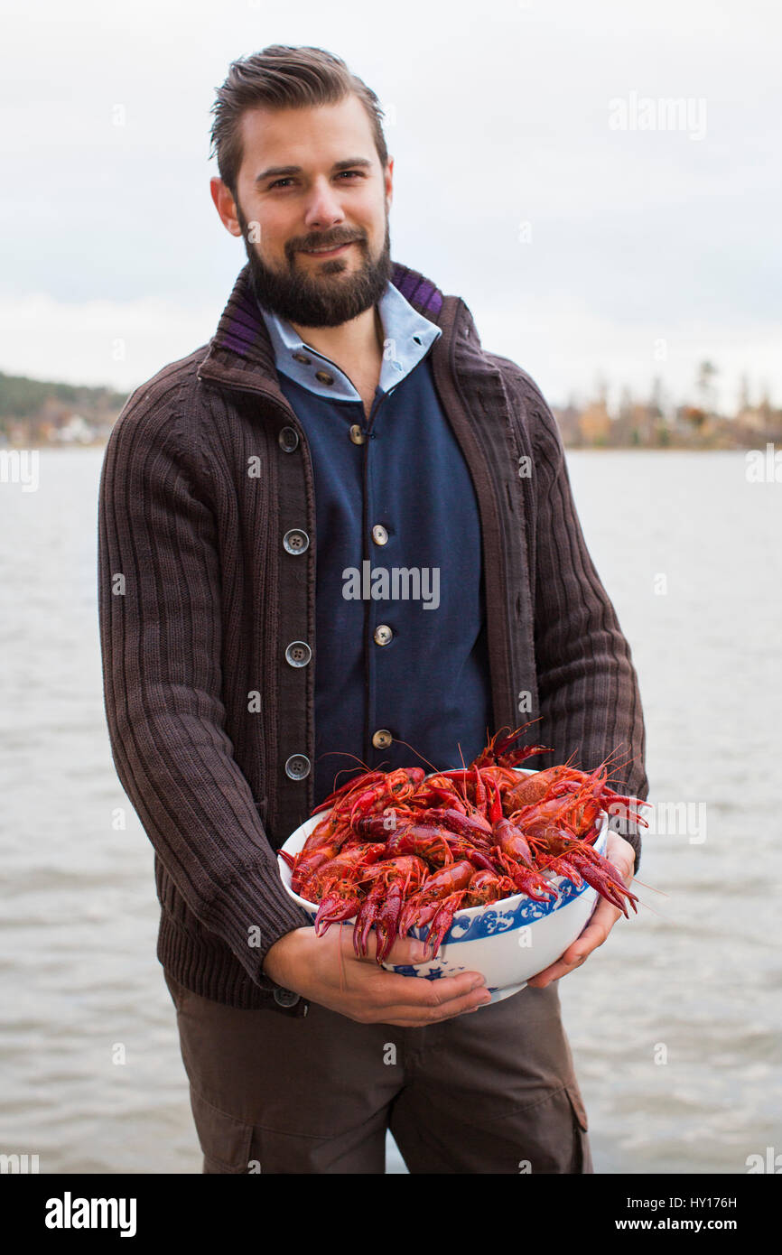 Sweden, Medelpad, Juniskar, Portrait of mid adult man holding bowl of crayfish (Astacidae) Stock Photo