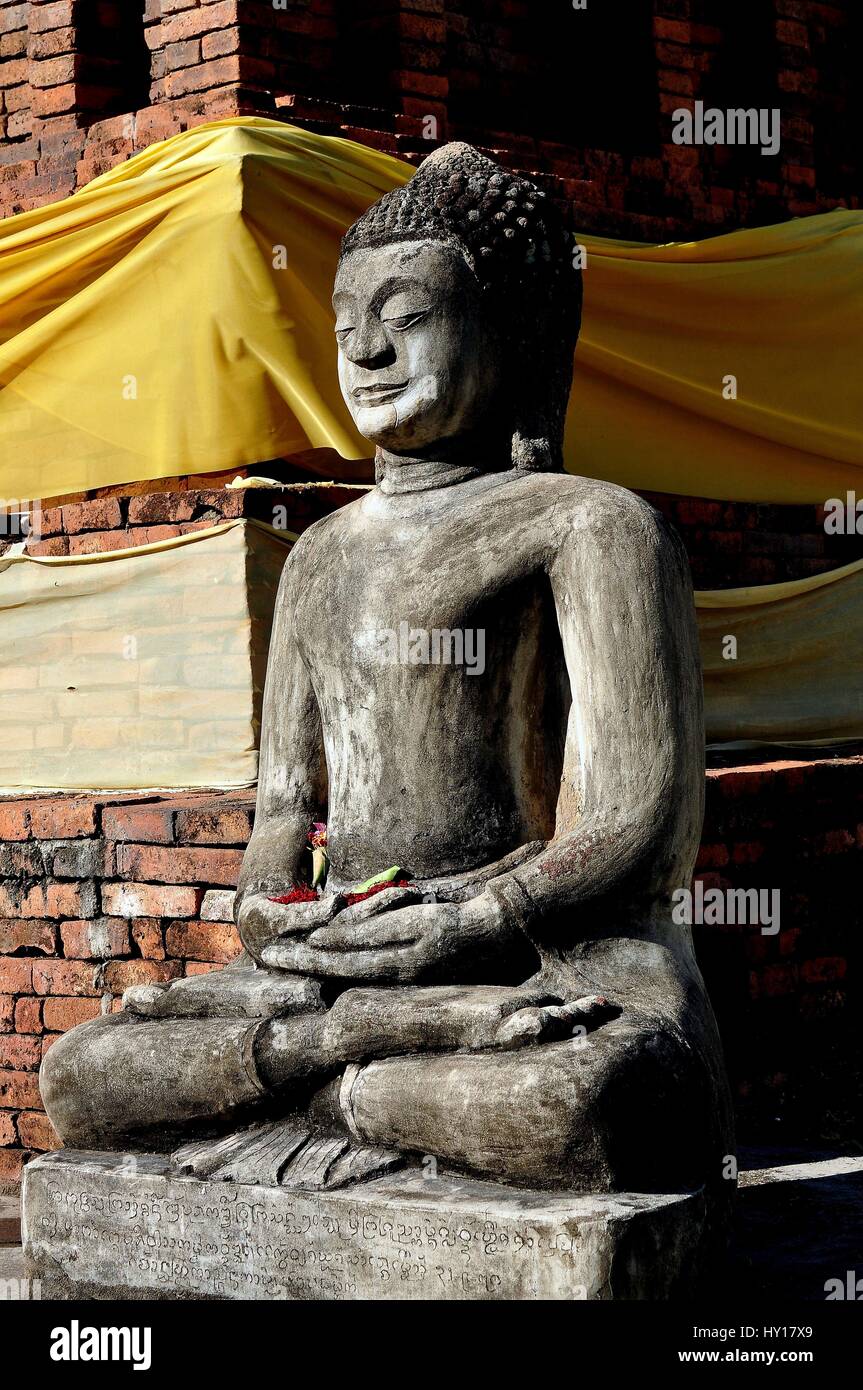 Lamphun, Thailand - December 28, 2012:   A serene sitting stone Buddha at the base of the Suwanna Chedi at Wat Phra That Haripunchai Maha Viham Stock Photo