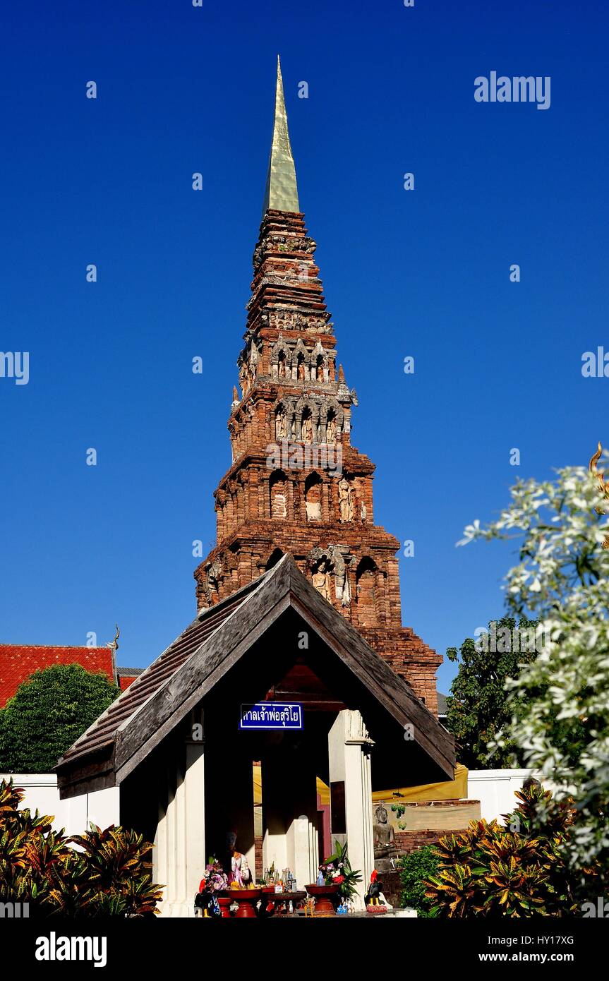 Lamphun, Thailand - December 28, 2012:  The Suwanna Chedi and Buddha shrine with offerings at Wat Phra That Haripunchai Maha Viram Stock Photo
