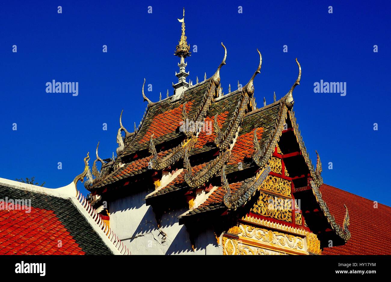 Lamphun, Thailand - December 28, 2012:  Gabled, interlocking, tiled roofs with ornamental chofahs atop the Ubosot at Wat Phra That Haripunchai Maha Vi Stock Photo