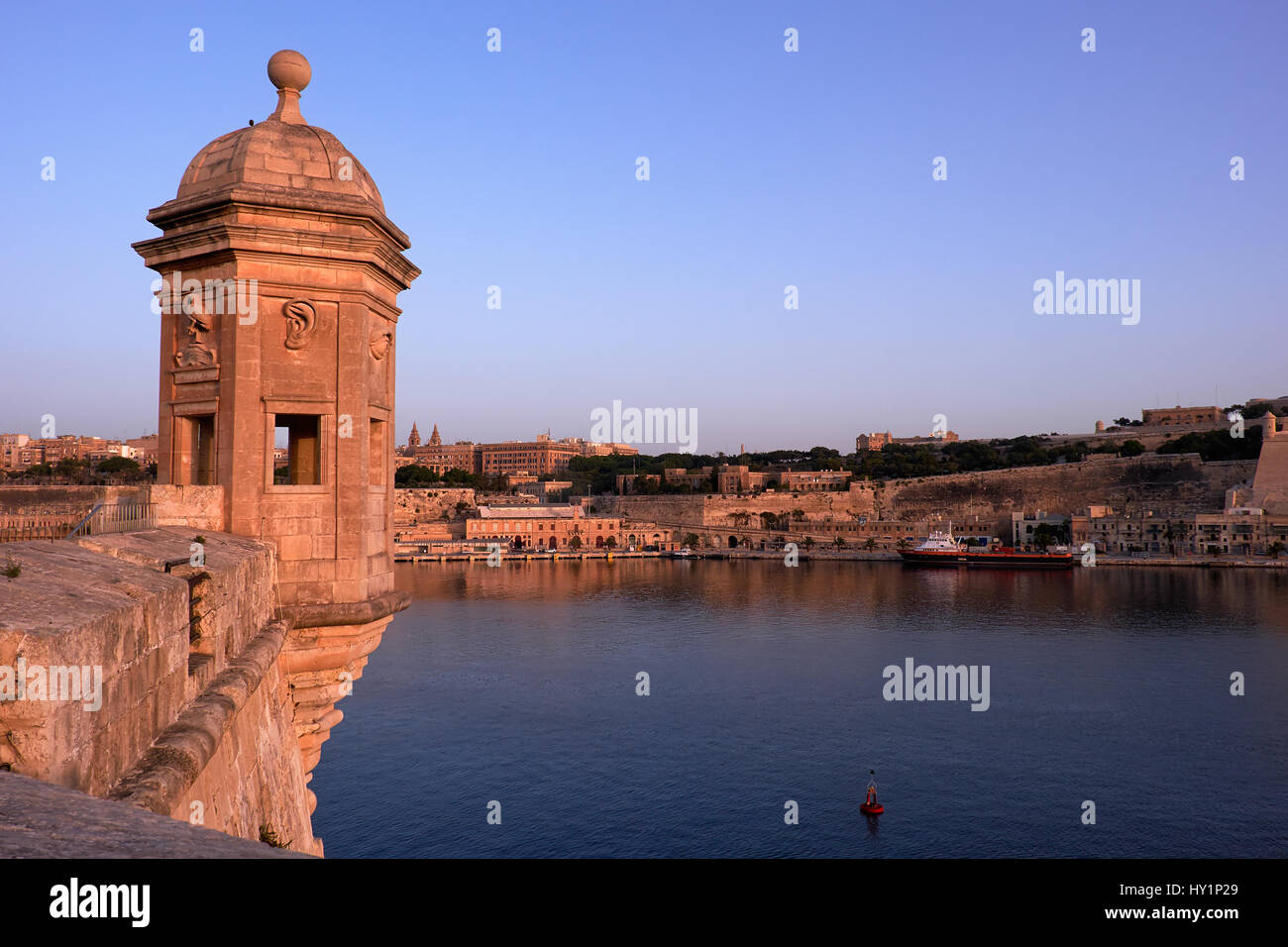 The early morning view of the Senglea Guard tower with sculpted symbols  (crane bird, ear and nose) on the background of Grand harbour. Senglea, Malta Stock Photo
