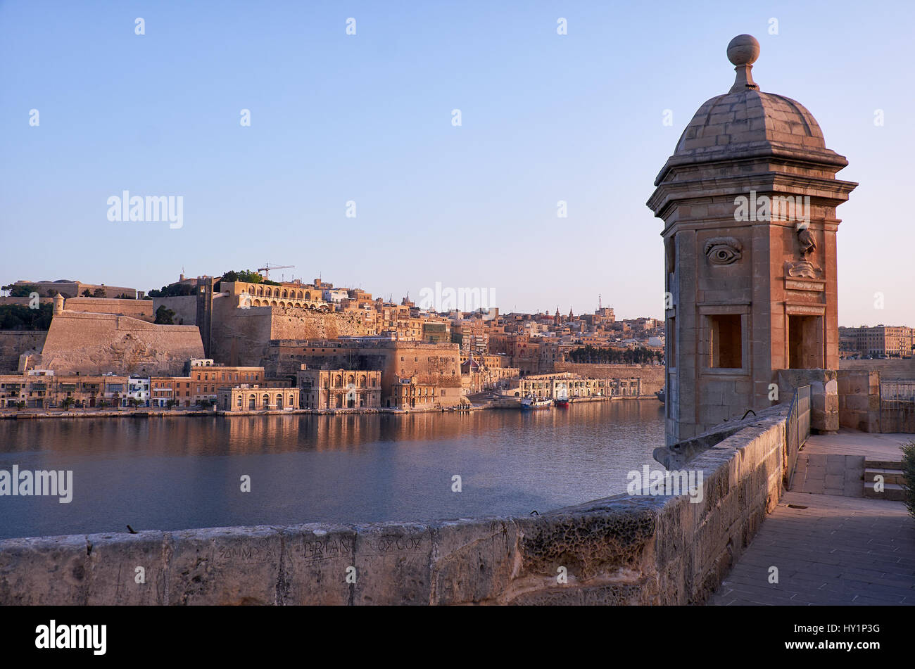 The early morning view of the Senglea Guard tower with sculpted symbols  (crane bird and ear) on the background of Grand harbour and Valletta. Senglea Stock Photo