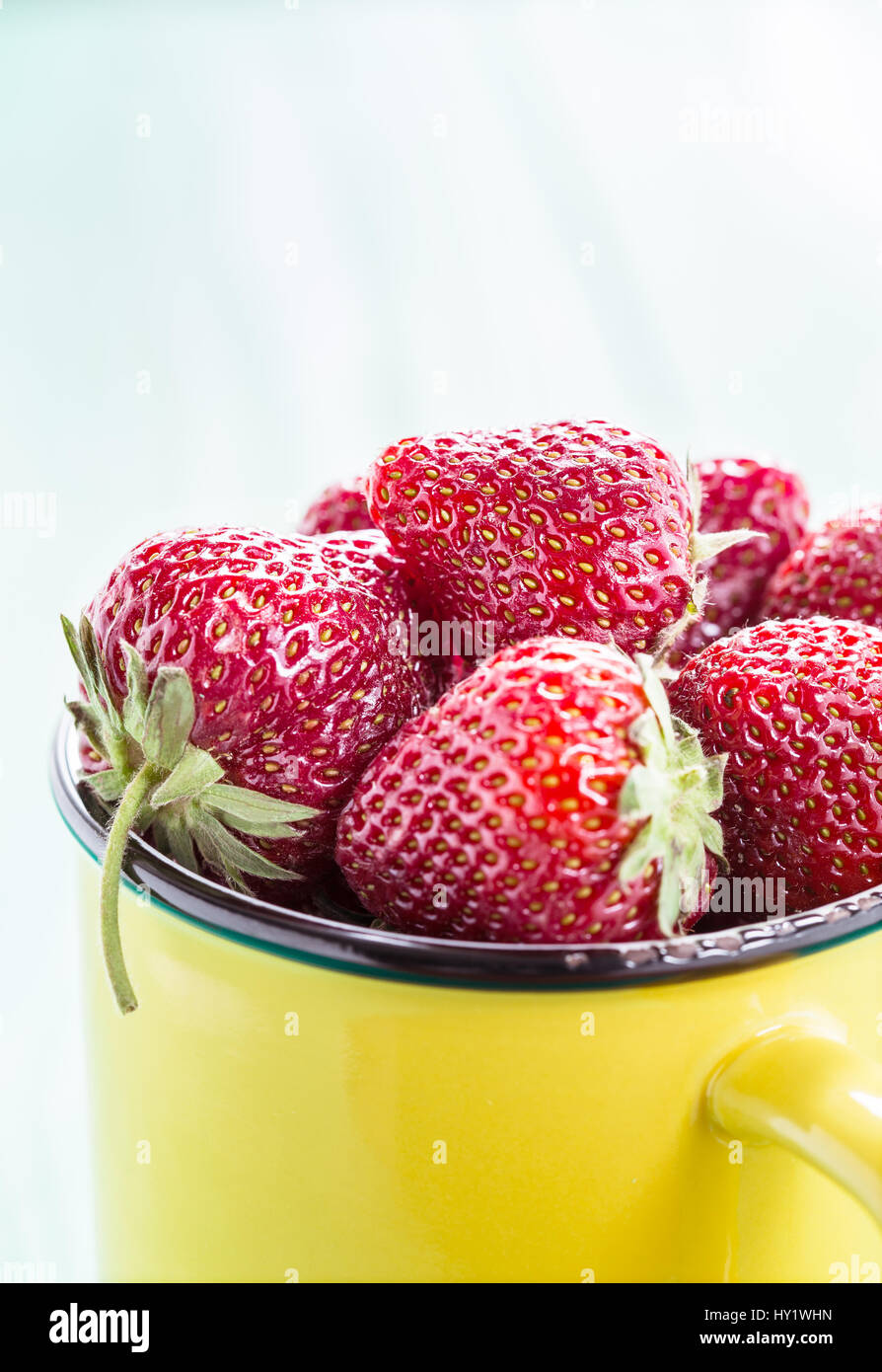 Fresh strawberries in a yellow cup on wooden table Stock Photo